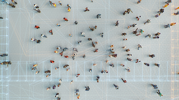Top-down view of people walking in different directions on a pale surface, overlaid with a network of white and orange lines connecting various points, indicating movement tracking or spatial data analysis..