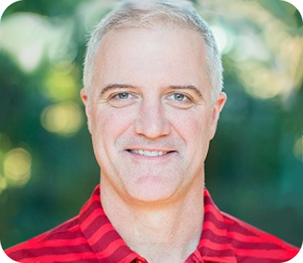Person wearing a red and black striped collared shirt, outdoors with a blurred green background.