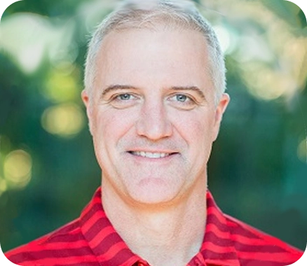 Person wearing a red and black striped collared shirt, outdoors with a blurred green background.